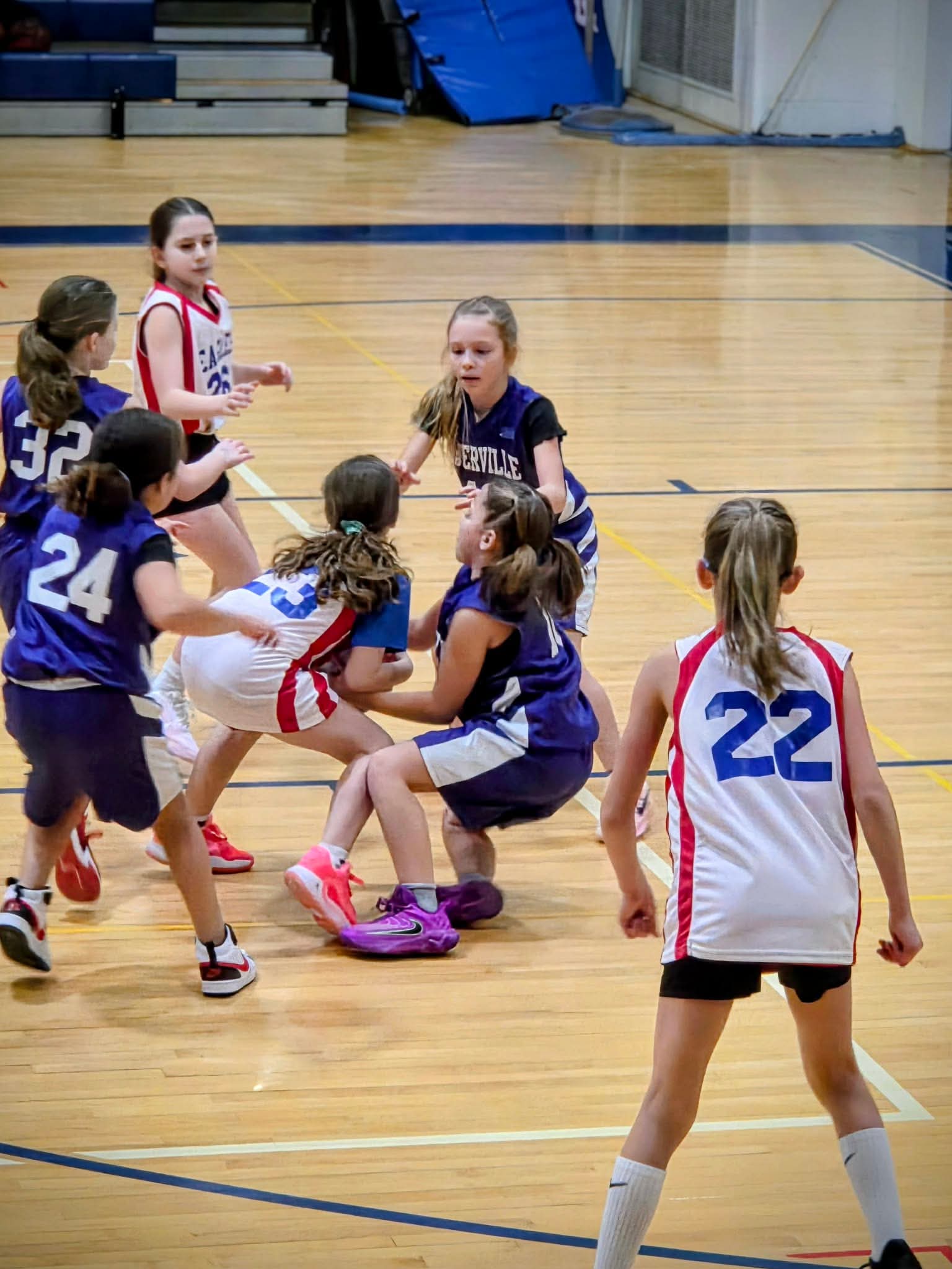 Two female youth basketball teams scramble for the ball during a game.