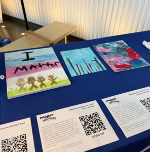 Various art media and information about Project Soul Chains are lying on a table with a blue tablecloth.